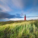 Scherpte en scherptediepte: hoe krijg je controle over wat scherp is en wat niet Rode vuurtoren op een met gras begroeide duin.